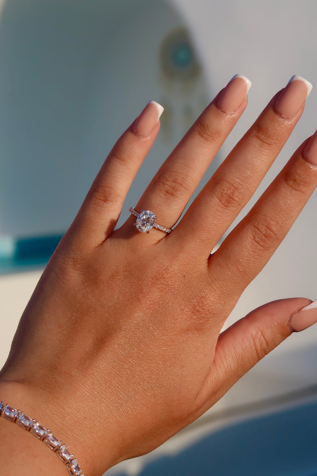 Hand with oval cut moissanite engagement ring against blue background demonstrating luxurious styling and brilliant light reflection