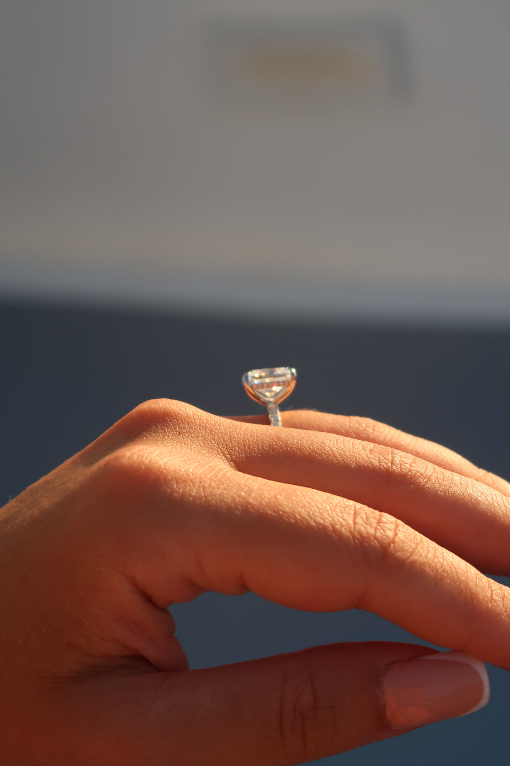 Close-up of radiant cut moissanite engagement ring on finger showing step cut faceting and hidden halo detail