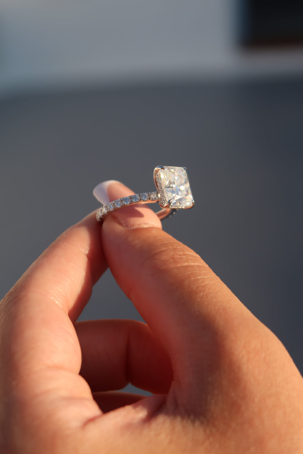 Hand holding radiant cut moissanite engagement ring in natural sunlight displaying fire and brilliance