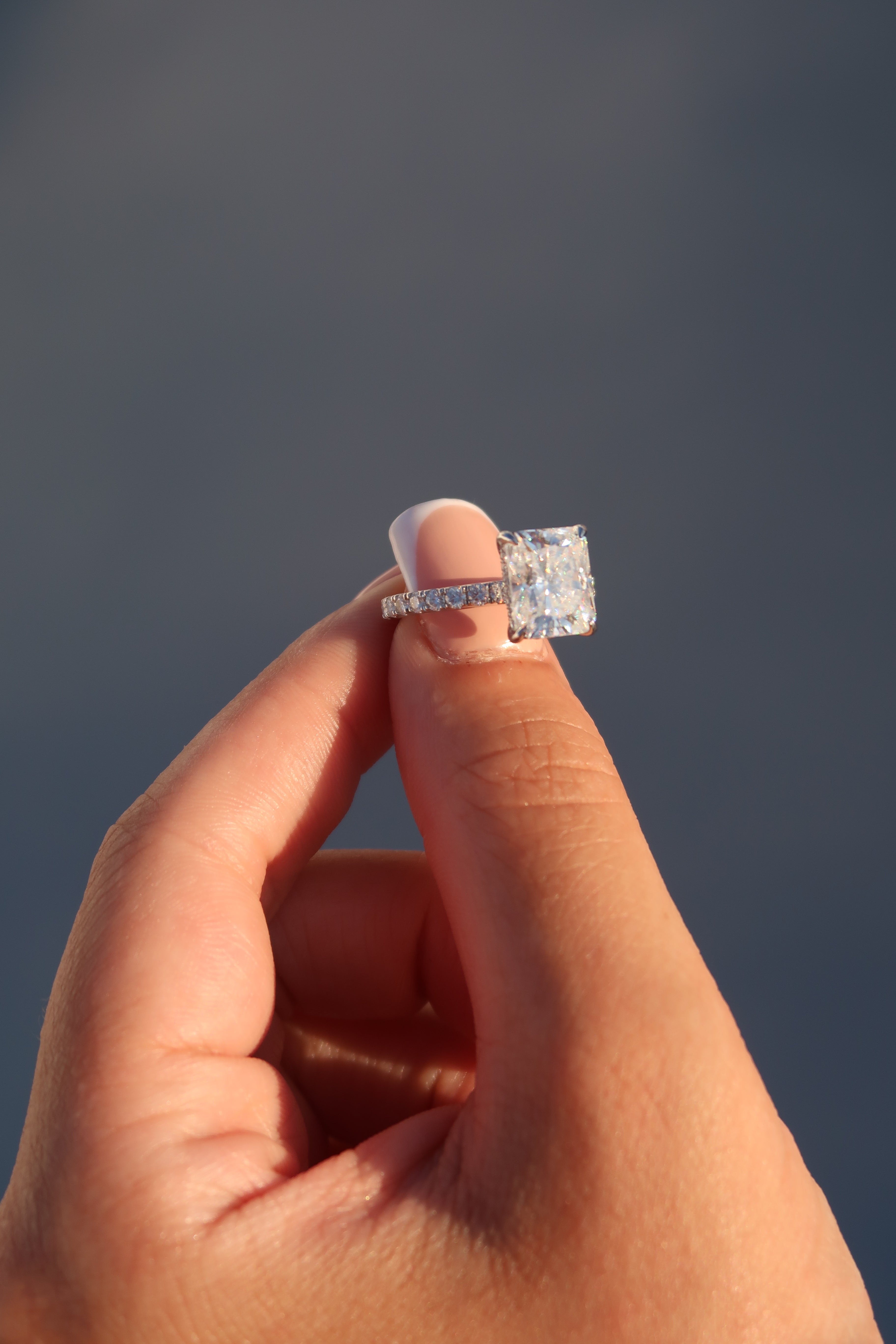 Hand wearing radiant cut moissanite engagement ring in outdoor setting showing elegant profile