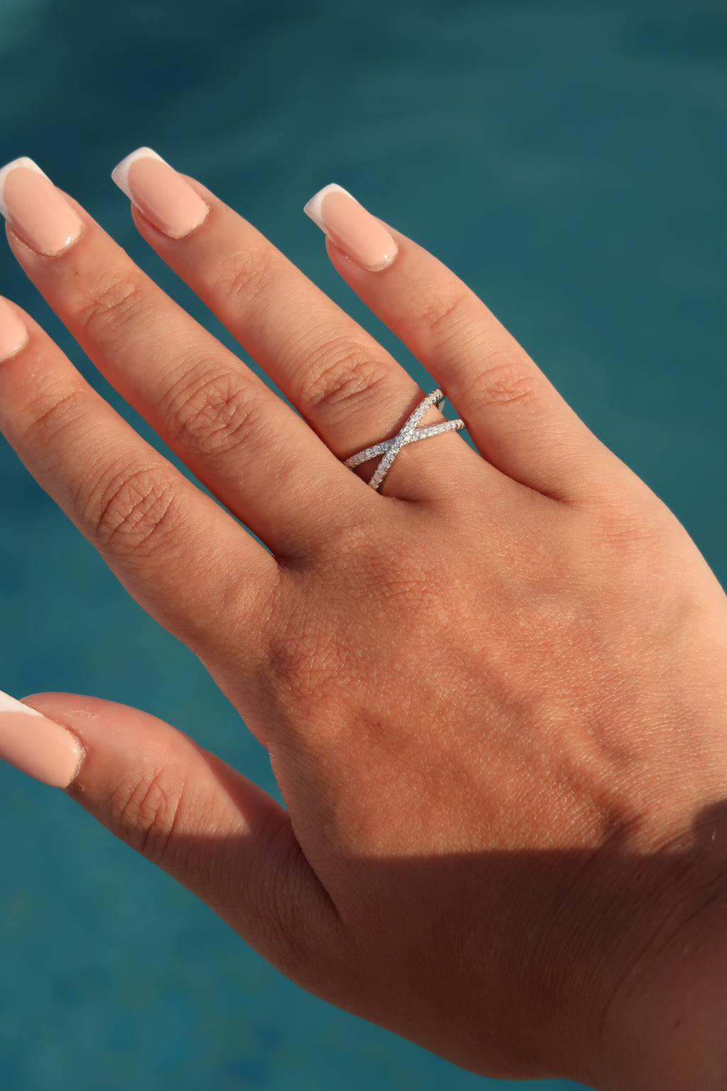 Hand displaying infinity crossover pavé moissanite wedding band against blue background showcasing intertwined pavé rows and elegant profile