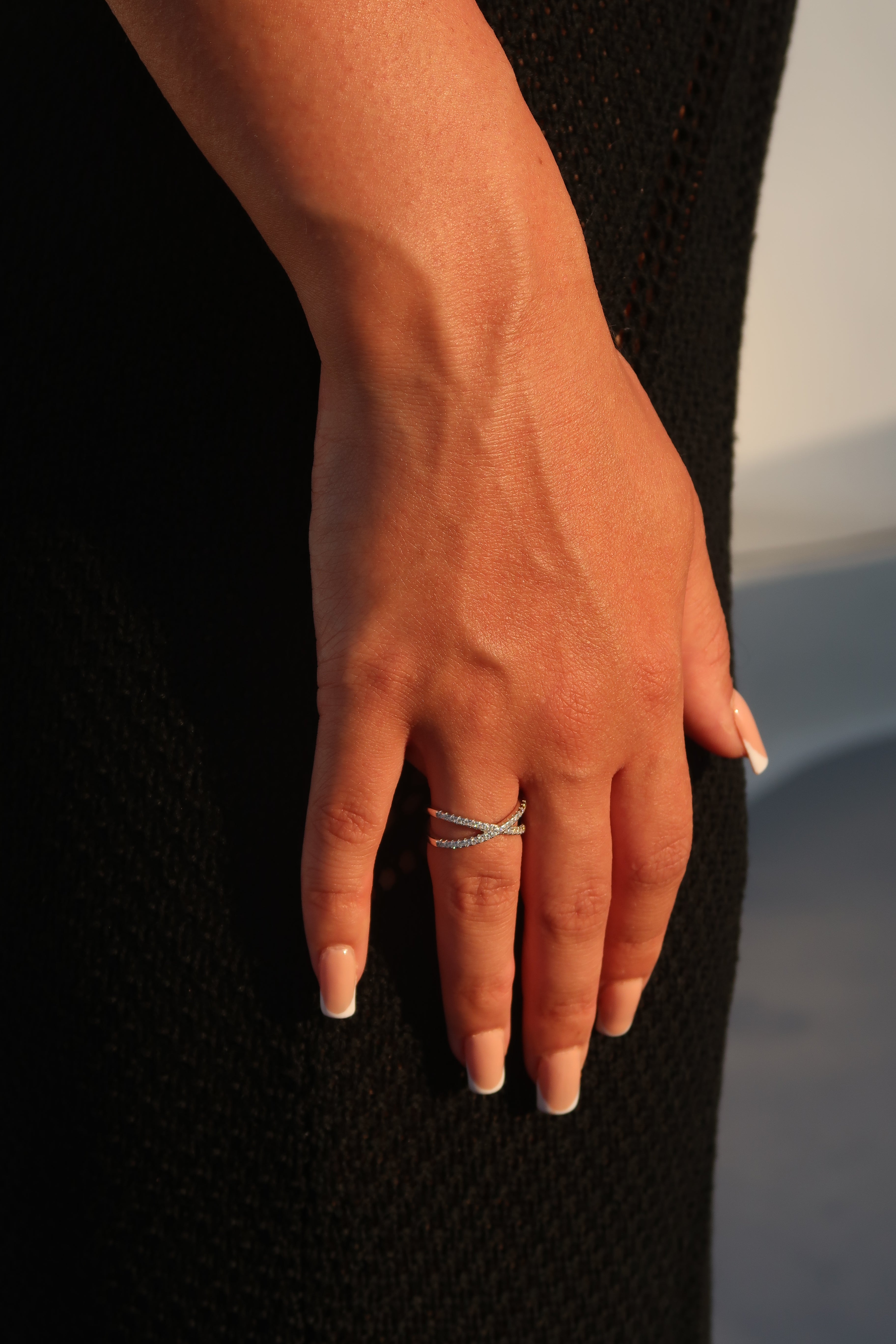 Hand with infinity crossover pavé moissanite wedding band against dark background demonstrating luxurious styling and light reflection