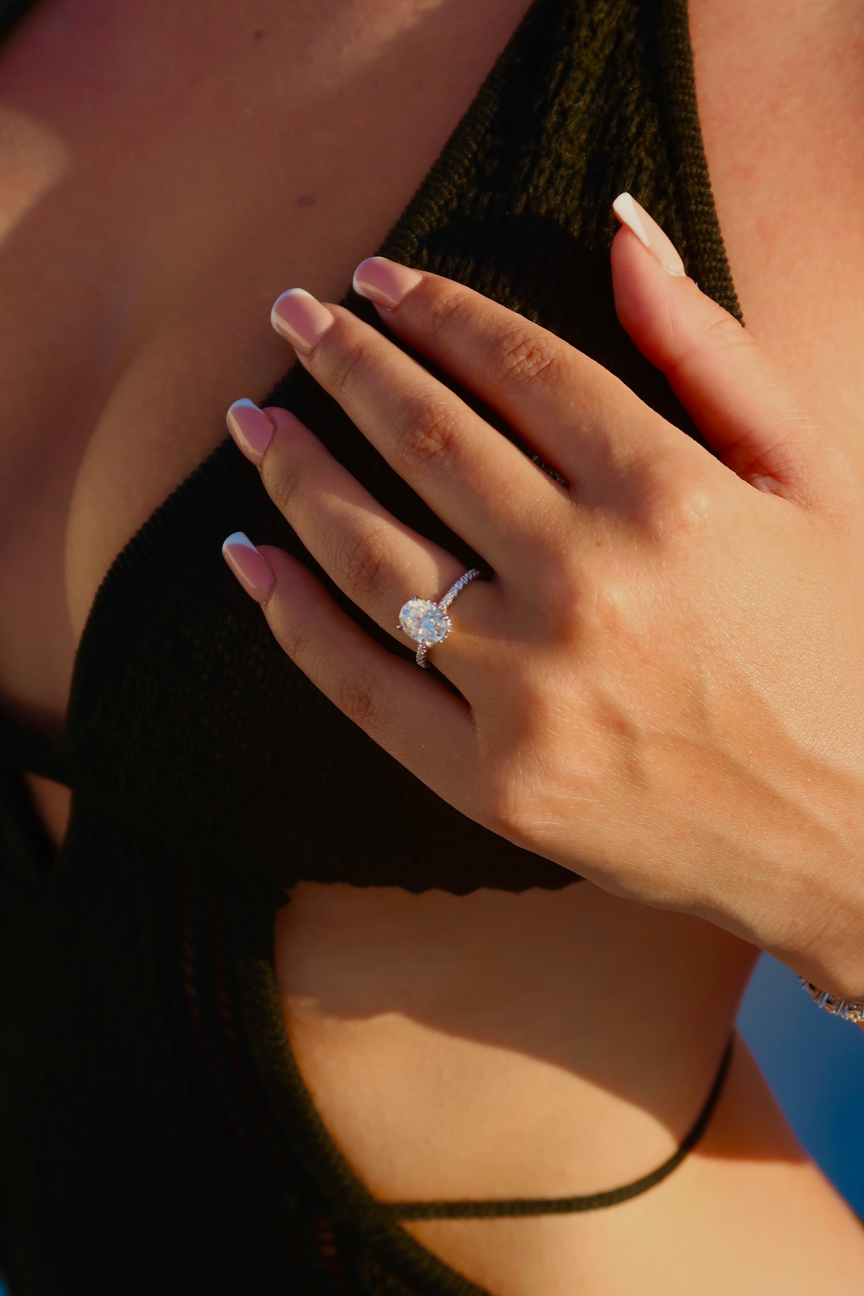 Hand wearing oval cut moissanite engagement ring with pavé band in dramatic lighting highlighting brilliant sparkle and elegant profile