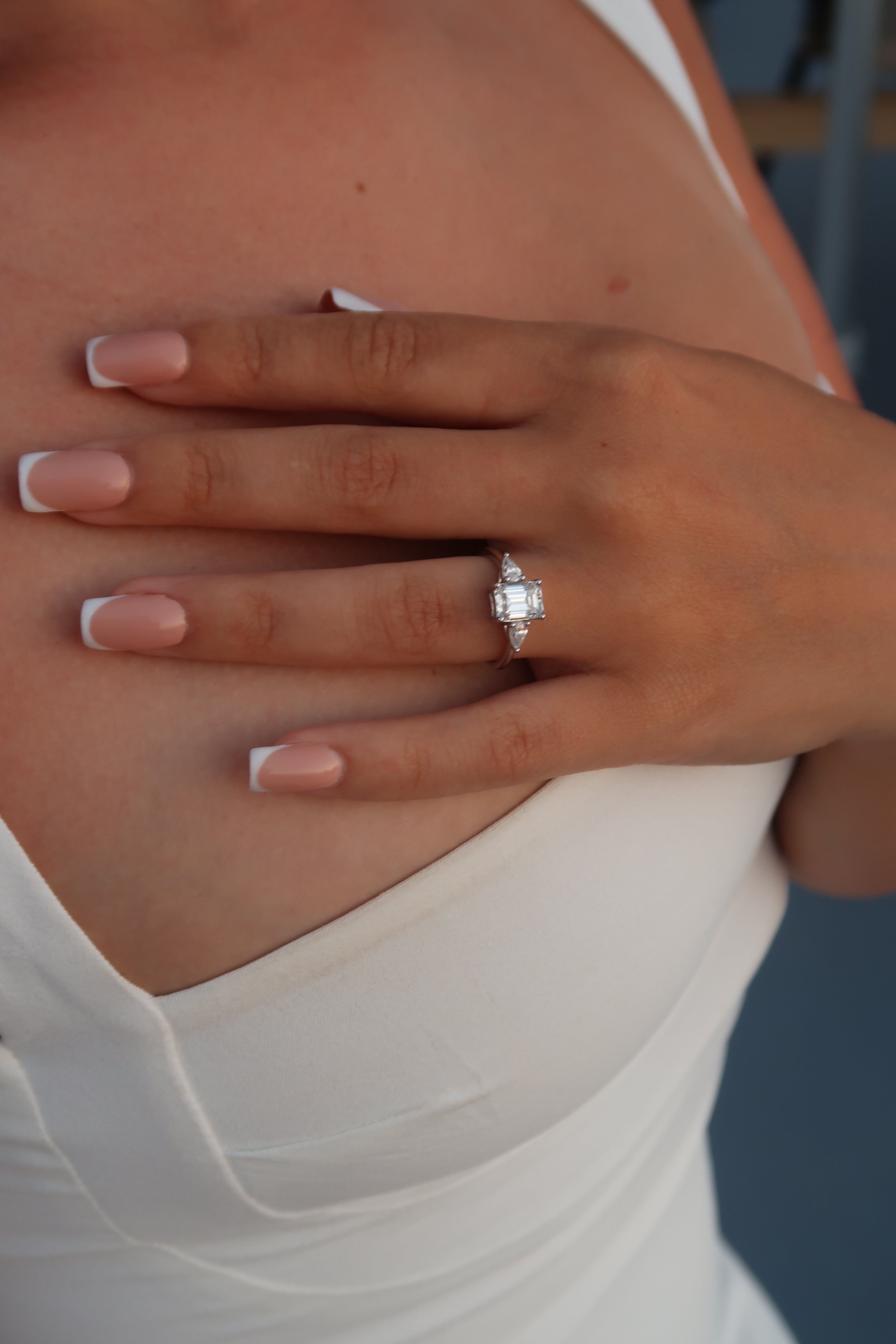 Emerald cut moissanite three-stone engagement ring with triangular side stones worn on hand with French manicure showcasing step cut center stone and elegant design