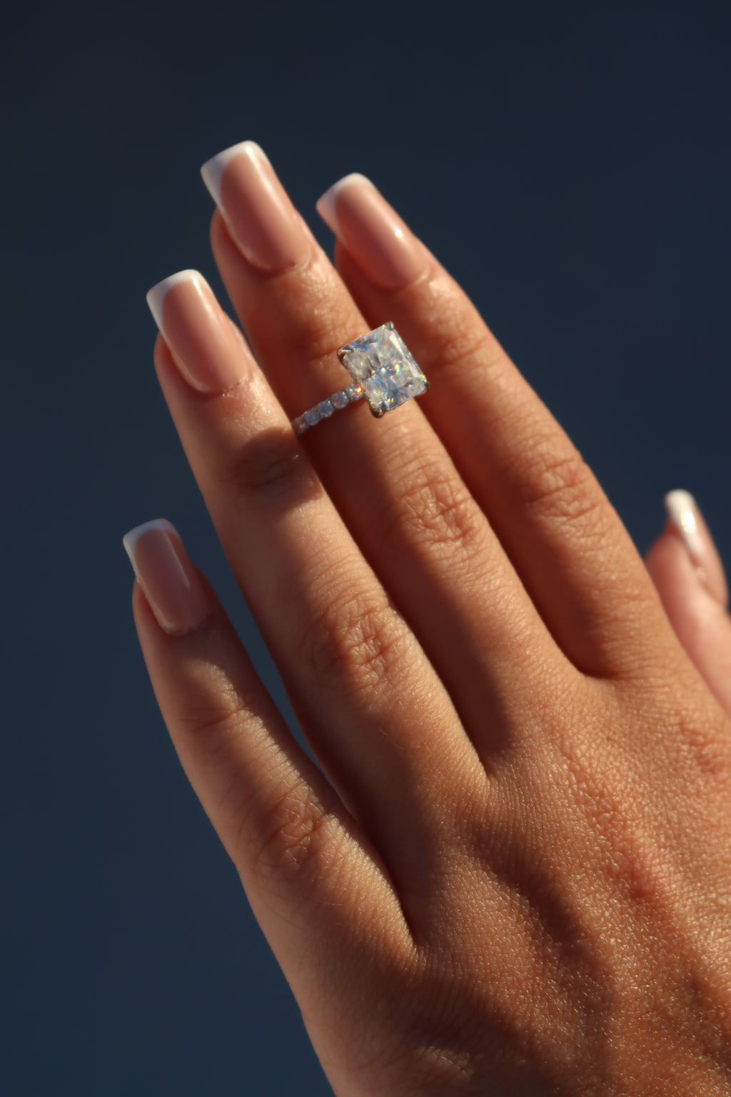 Hands displaying radiant cut moissanite engagement ring with dramatic lighting highlighting faceted stone