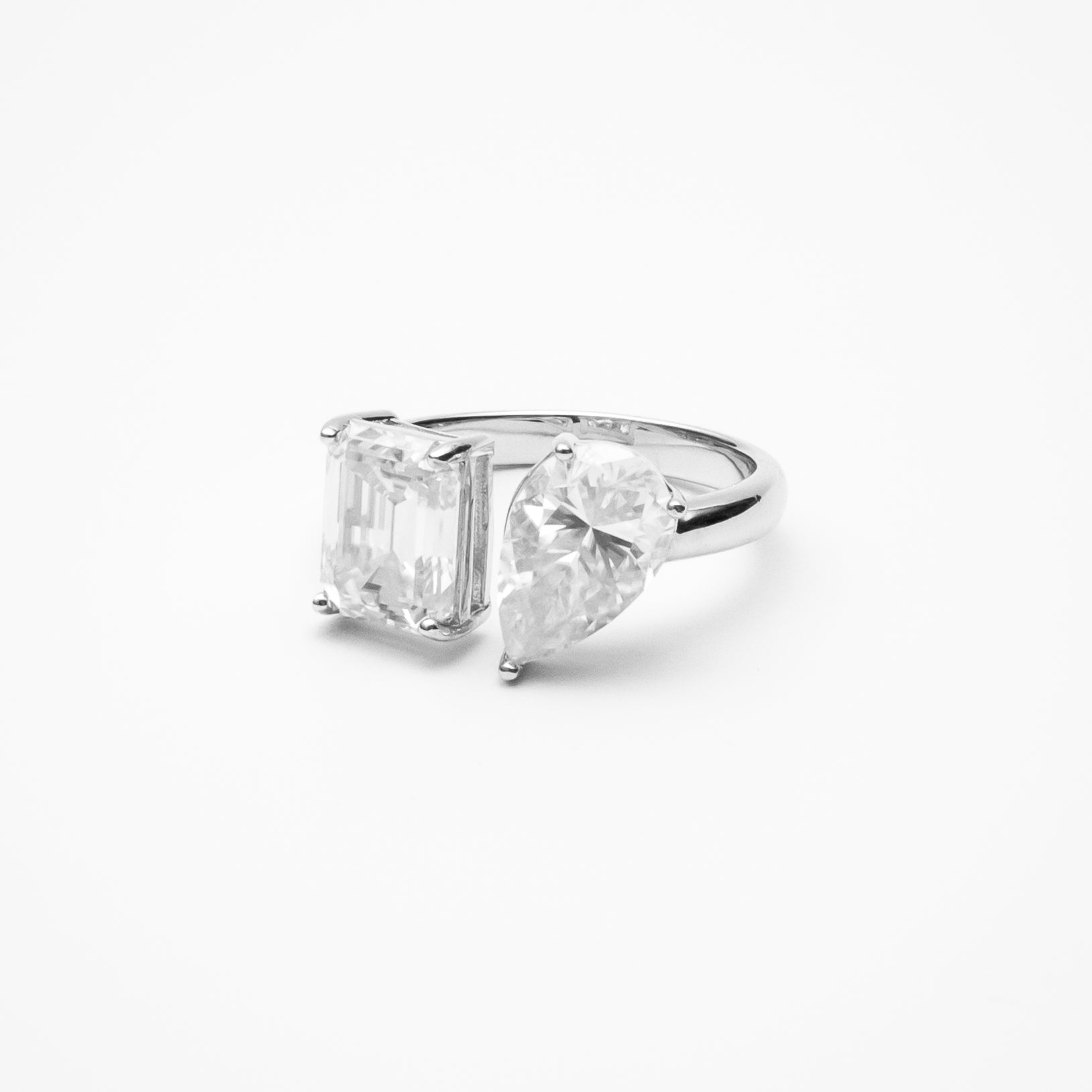 Toi et moi engagement ring with emerald cut and pear cut moissanite stones in white gold setting on clean white background showcasing dual stone design symbolizing unity