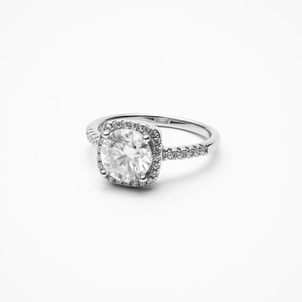 Cushion cut moissanite halo engagement ring with pavé band in white gold setting on clean white background