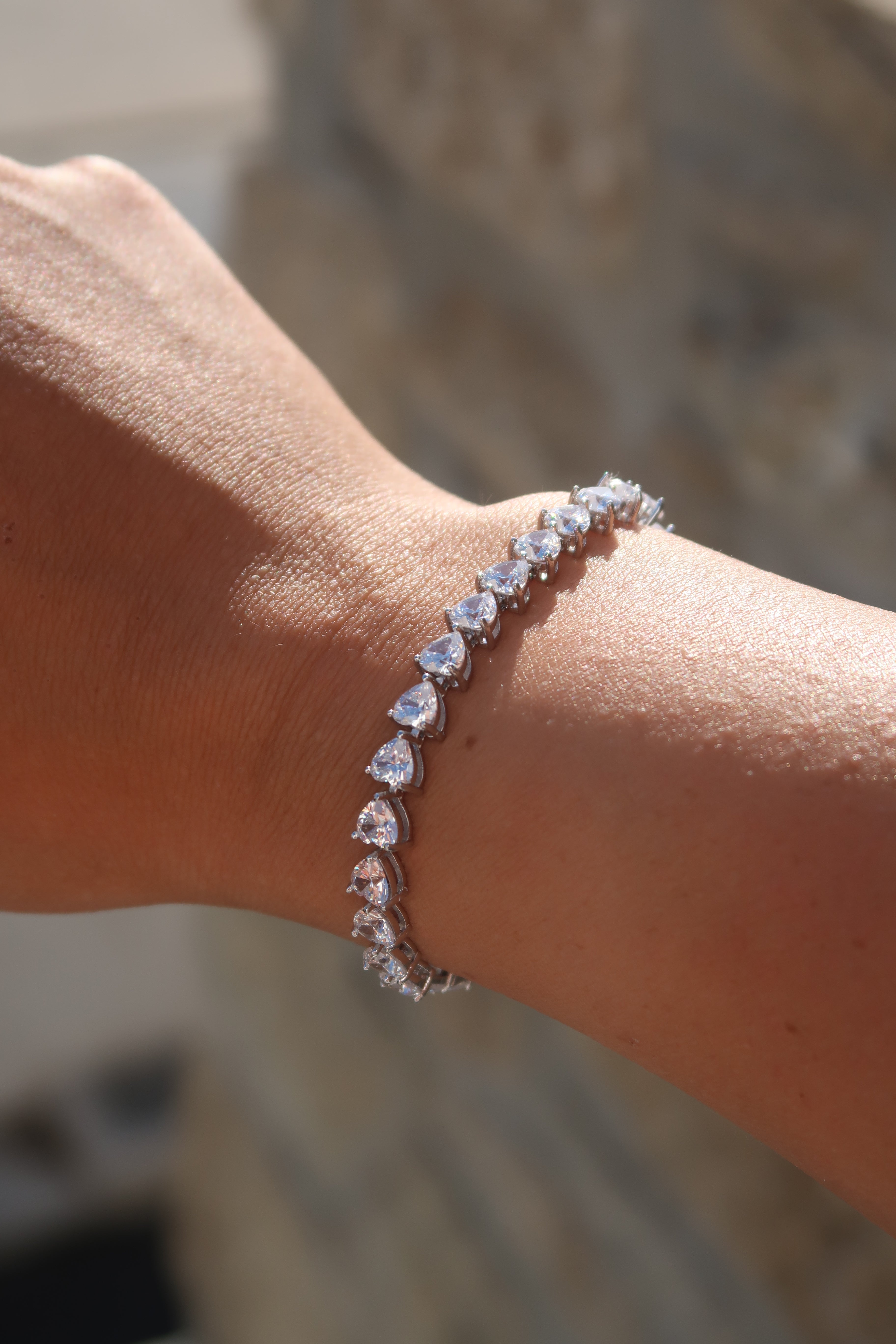 Heart cut moissanite tennis bracelet on wrist against textured background highlighting brilliant sparkle