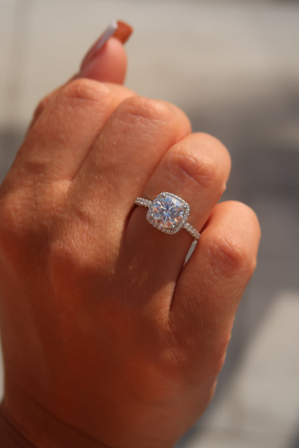 Close-up of hand with cushion cut moissanite halo engagement ring showcasing brilliant light reflection