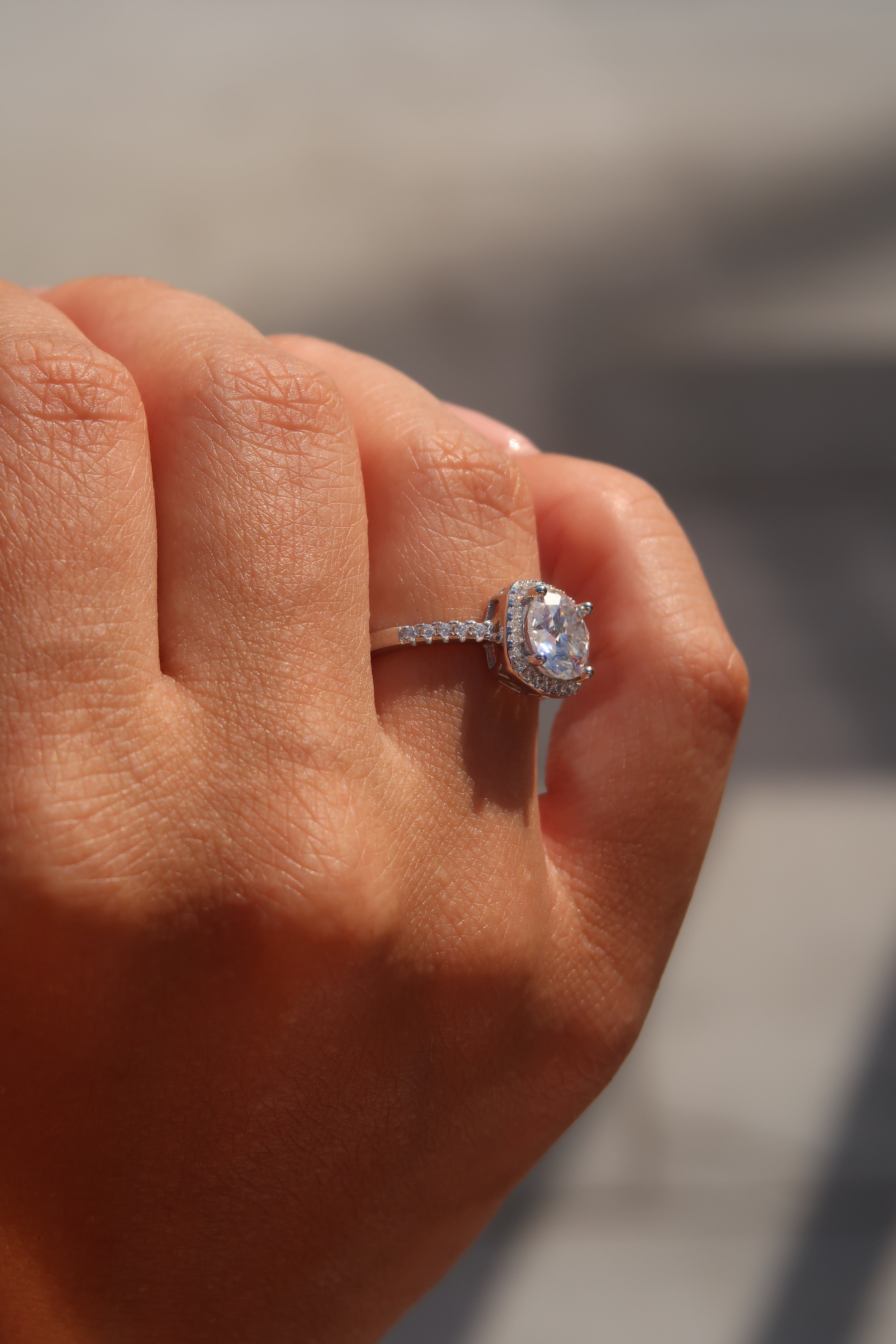 Hand wearing cushion cut moissanite halo engagement ring in natural lighting displaying fire and sparkle