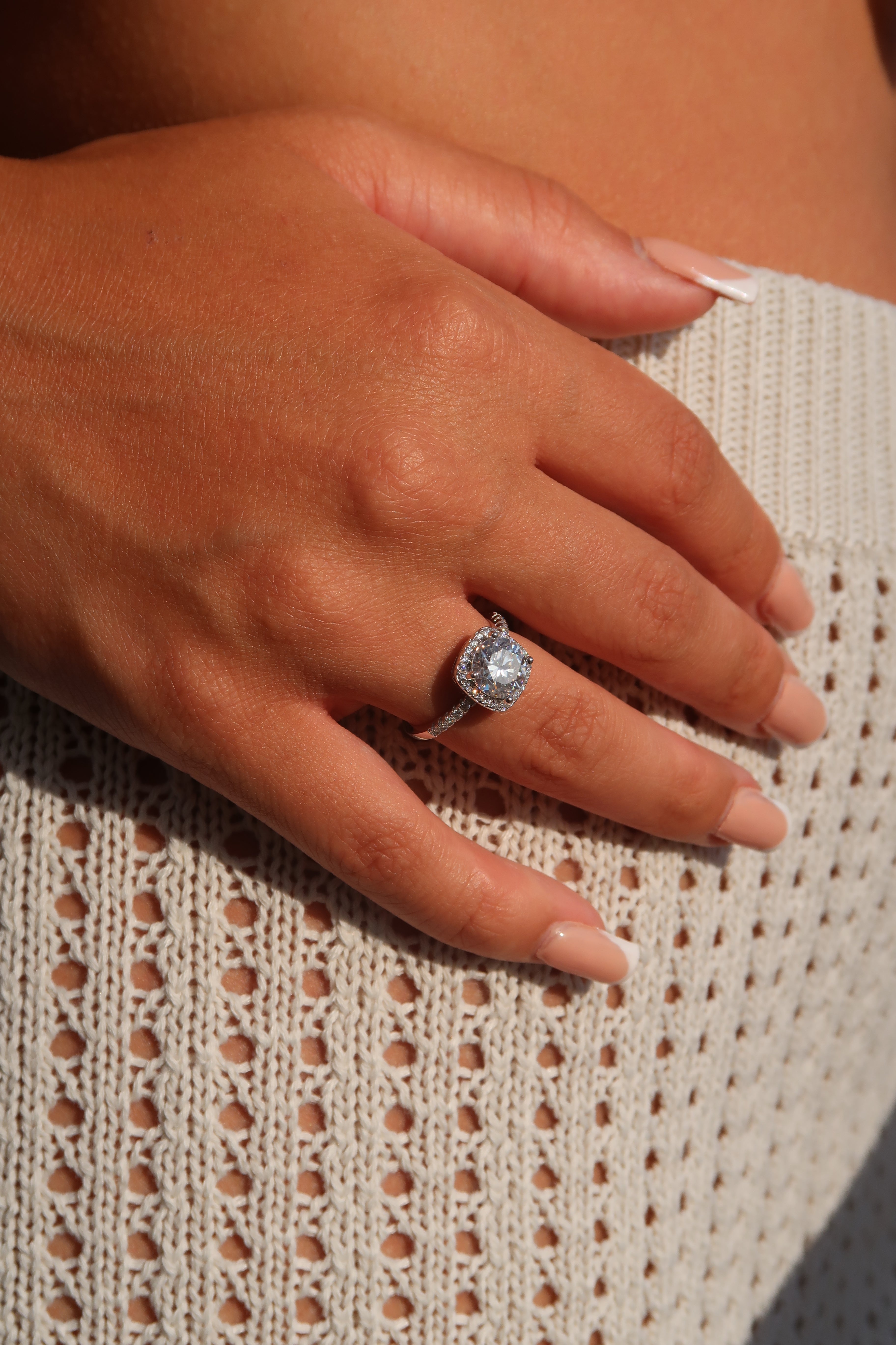 Hand wearing cushion cut moissanite halo engagement ring on textured fabric showcasing brilliant center stone and halo detail
