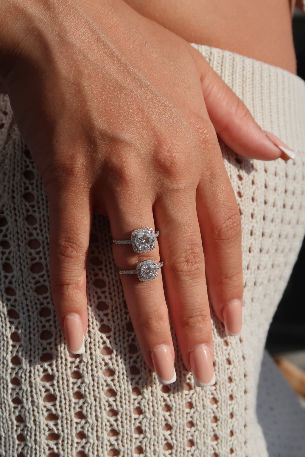 Hand wearing cushion cut moissanite halo engagement ring on knitted fabric demonstrating everyday elegance