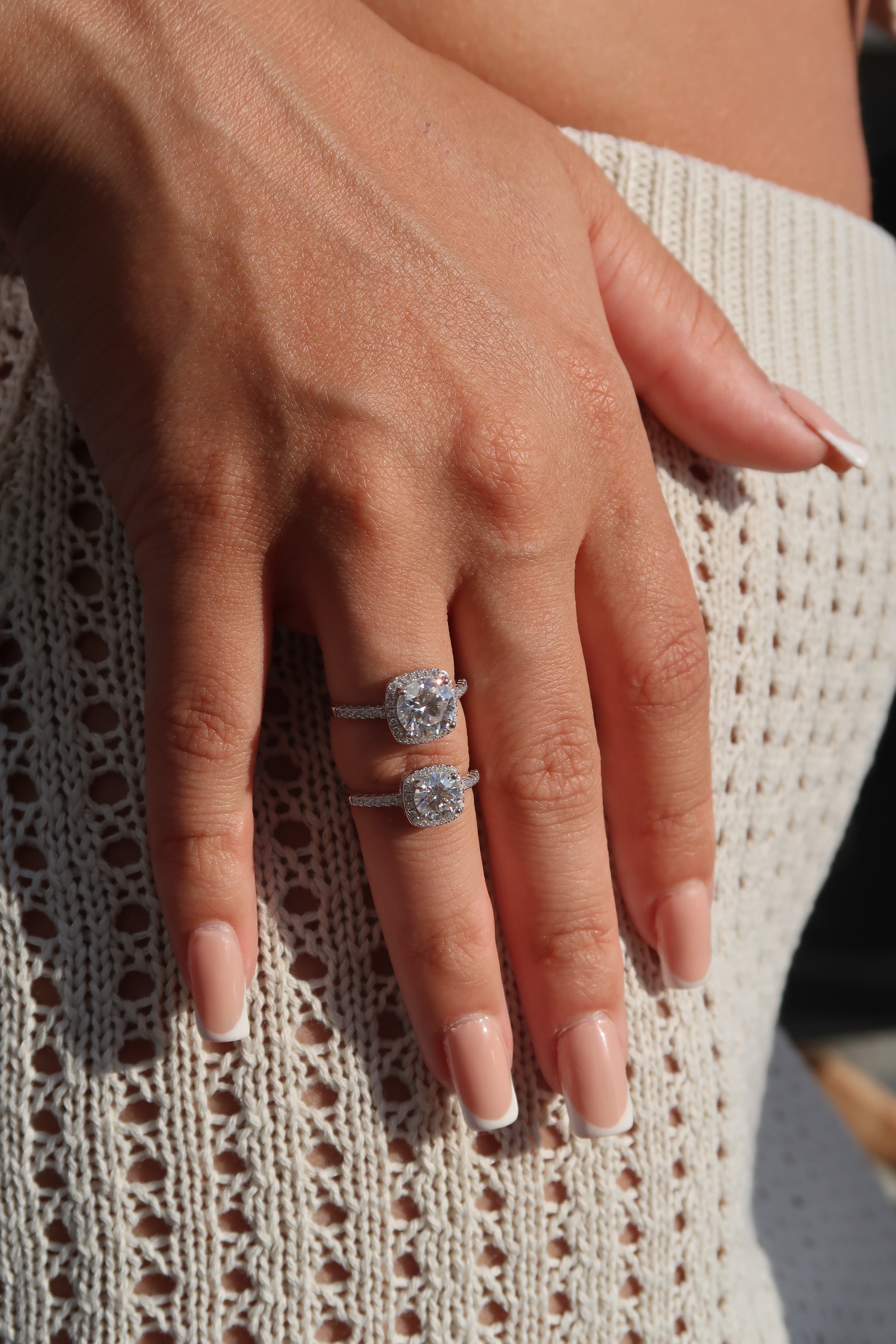 Hand wearing cushion cut moissanite halo engagement ring on knitted fabric demonstrating everyday elegance