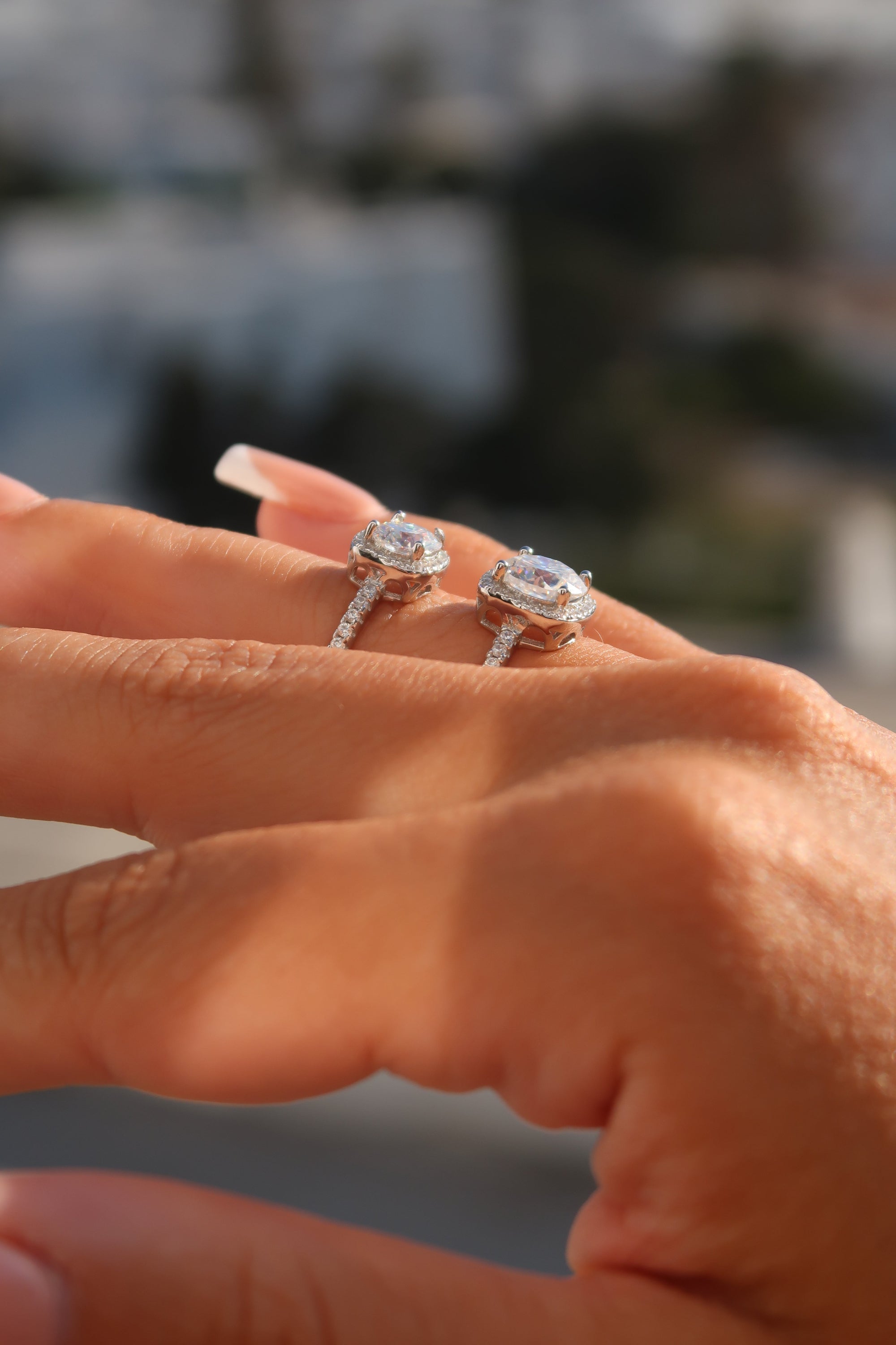 Hand wearing cushion cut moissanite halo engagement ring in outdoor setting highlighting luxurious sparkle