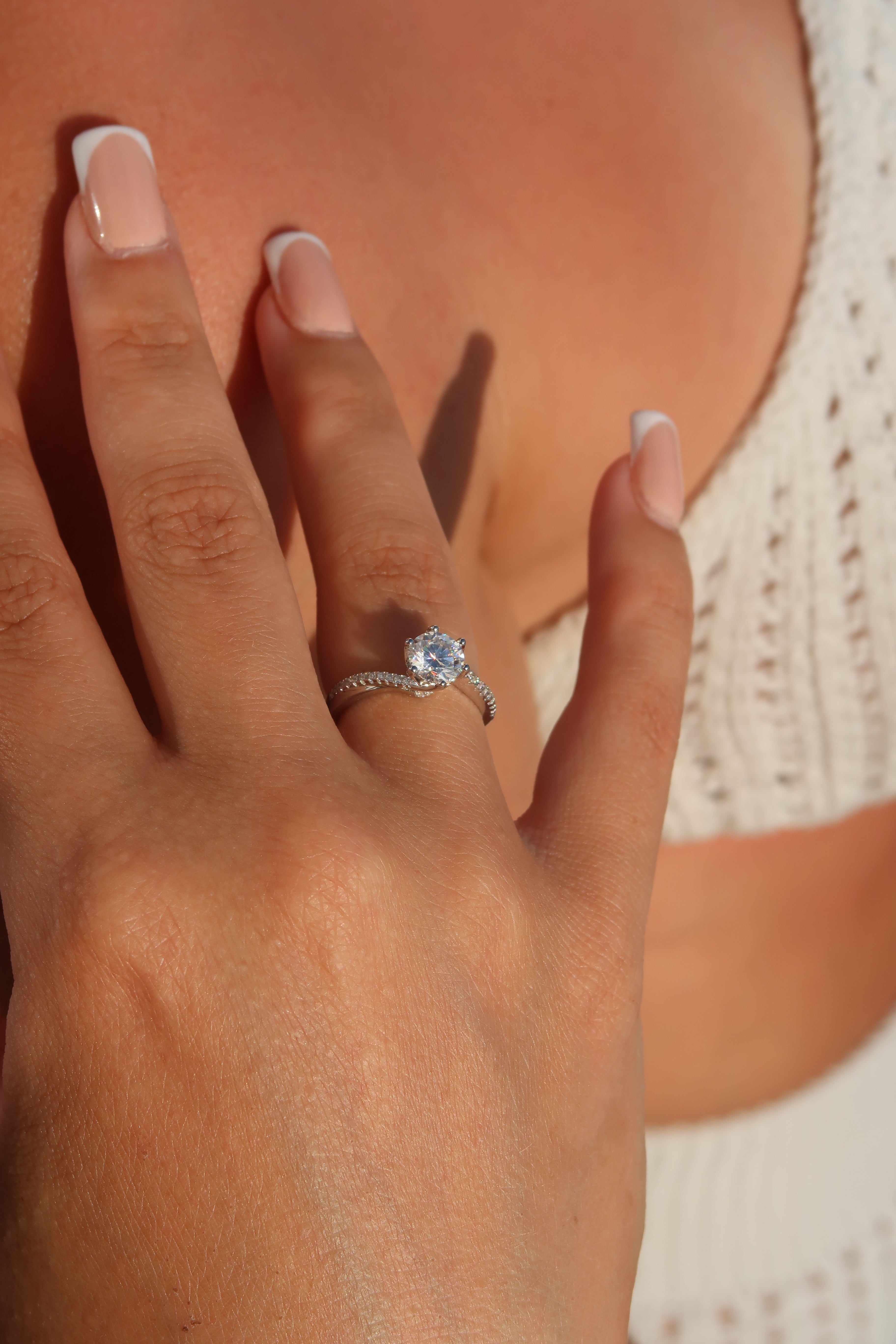 Hand with round cut moissanite engagement ring showing twisted pavé band design and brilliant center stone