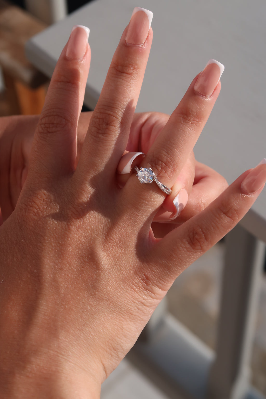 Hands displaying round cut moissanite engagement ring with twisted band in natural lighting emphasizing fire and brilliance