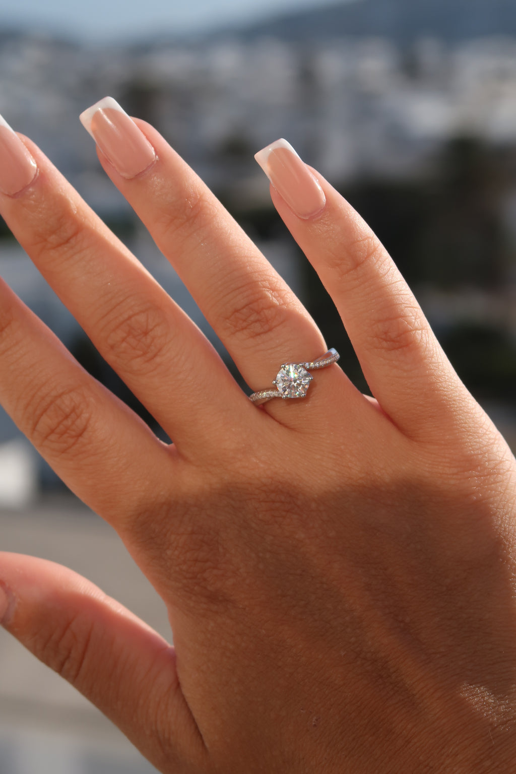 Hand wearing round cut moissanite engagement ring outdoors showcasing twisted pavé setting and elegant profile