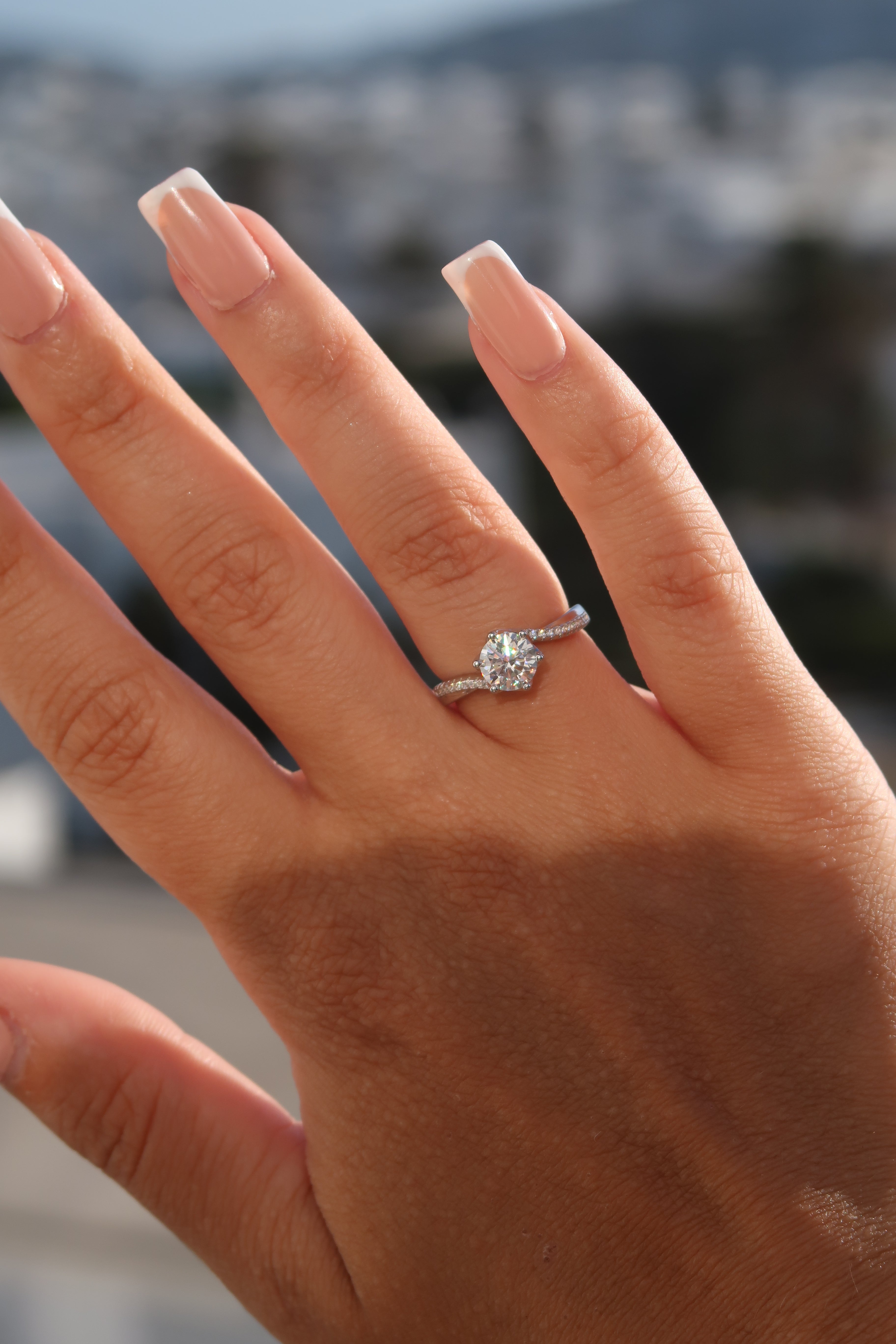 Hand wearing round cut moissanite engagement ring outdoors showcasing twisted pavé setting and elegant profile