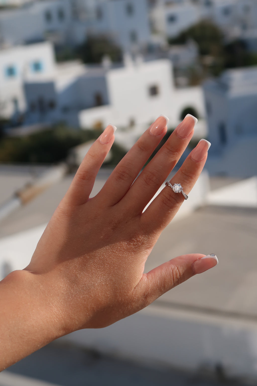 Hand with round cut moissanite engagement ring against coastal background demonstrating luxurious everyday styling