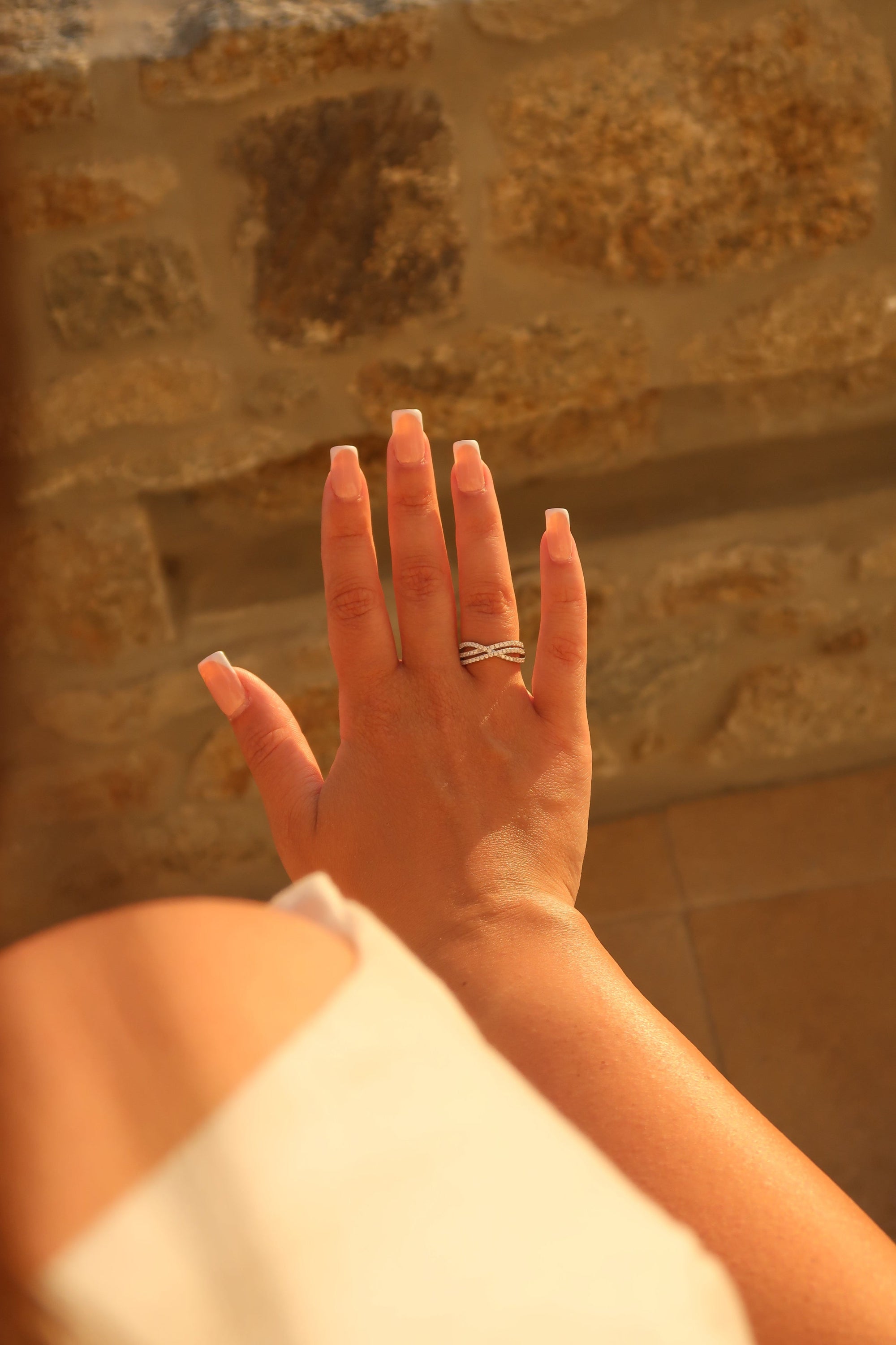 Hand with crossover pavé moissanite band against warm background highlighting intertwined band design