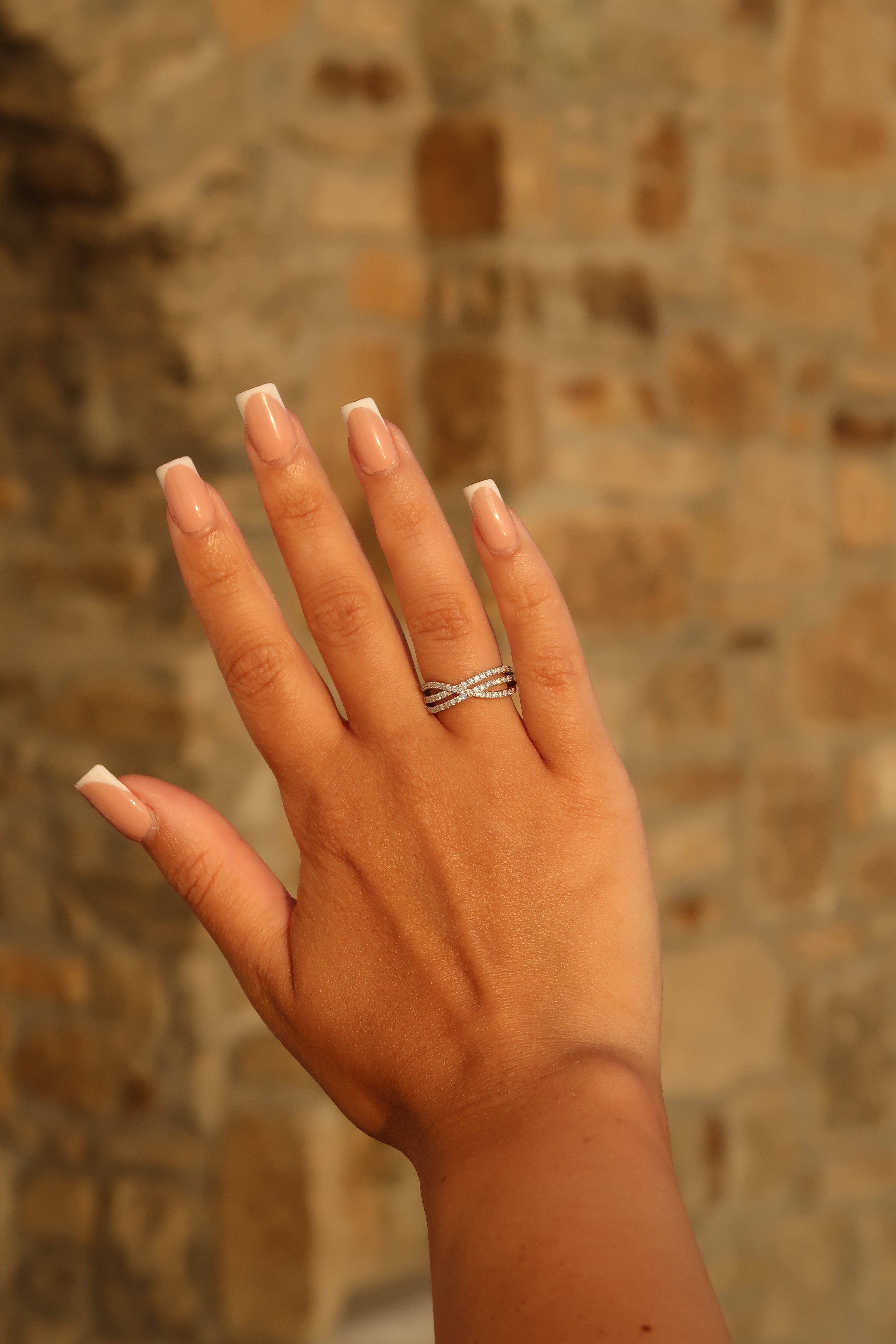 Hand with crossover pavé moissanite band against textured background showing versatile styling