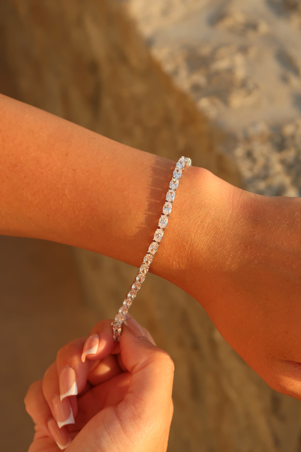 Hand wearing oval cut moissanite tennis bracelet in natural outdoor lighting showcasing brilliant fire and sparkle