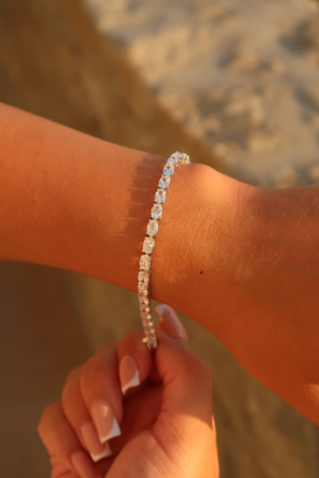 Hand wearing oval cut moissanite tennis bracelet in natural stone setting emphasizing timeless elegance