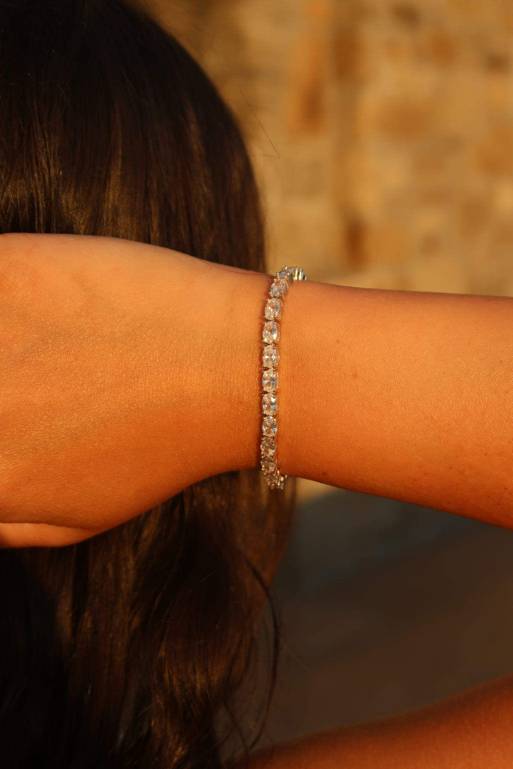 Oval cut moissanite tennis bracelet worn on wrist against warm background highlighting elegant oval stone shape