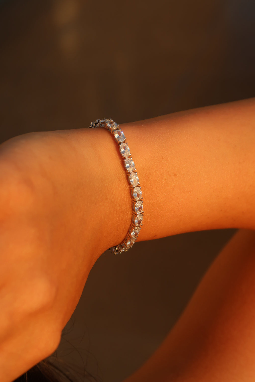 Hand with oval cut moissanite tennis bracelet in warm lighting showcasing continuous line of oval brilliance