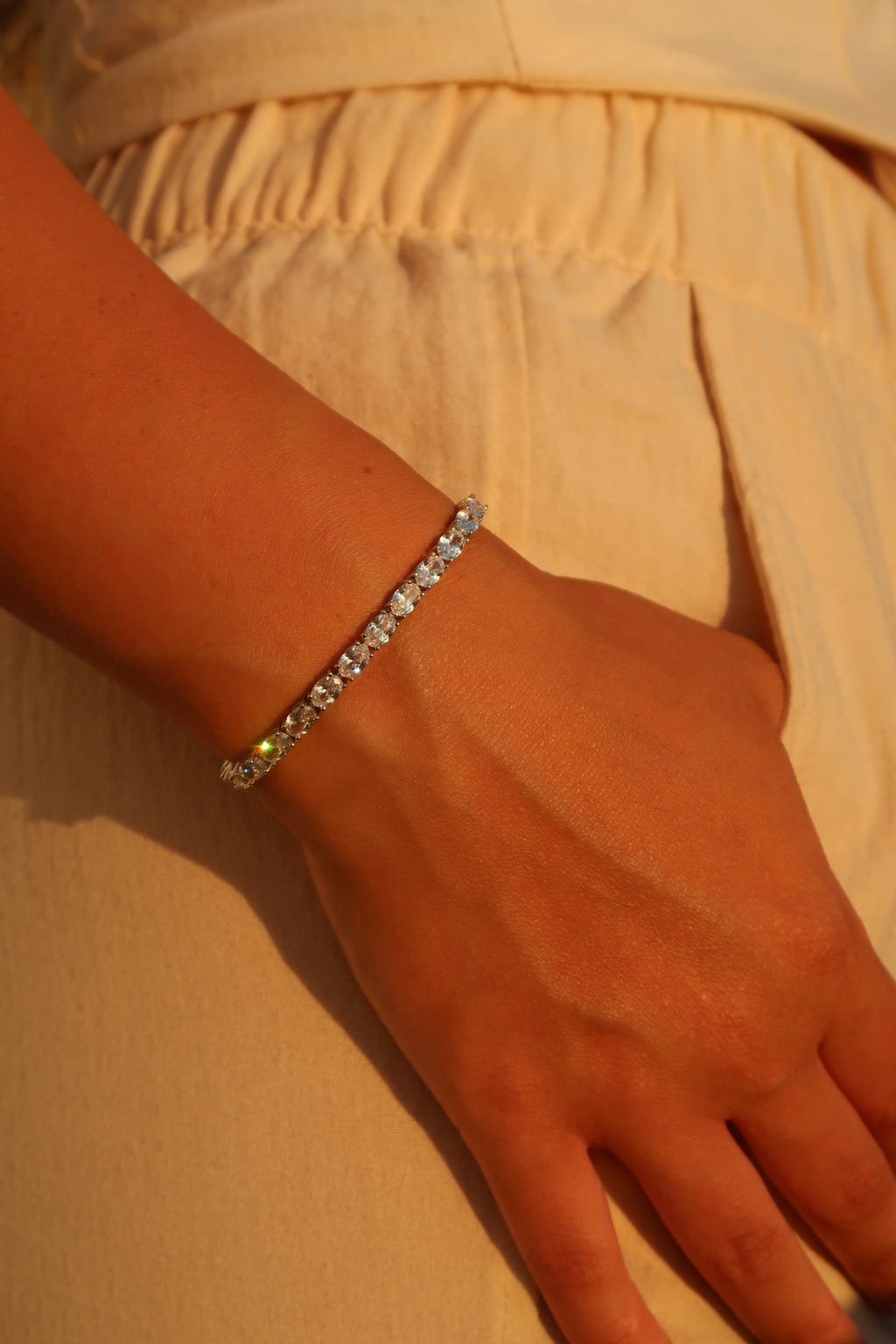 Hand with oval cut moissanite tennis bracelet in golden sunlight demonstrating luxurious everyday styling