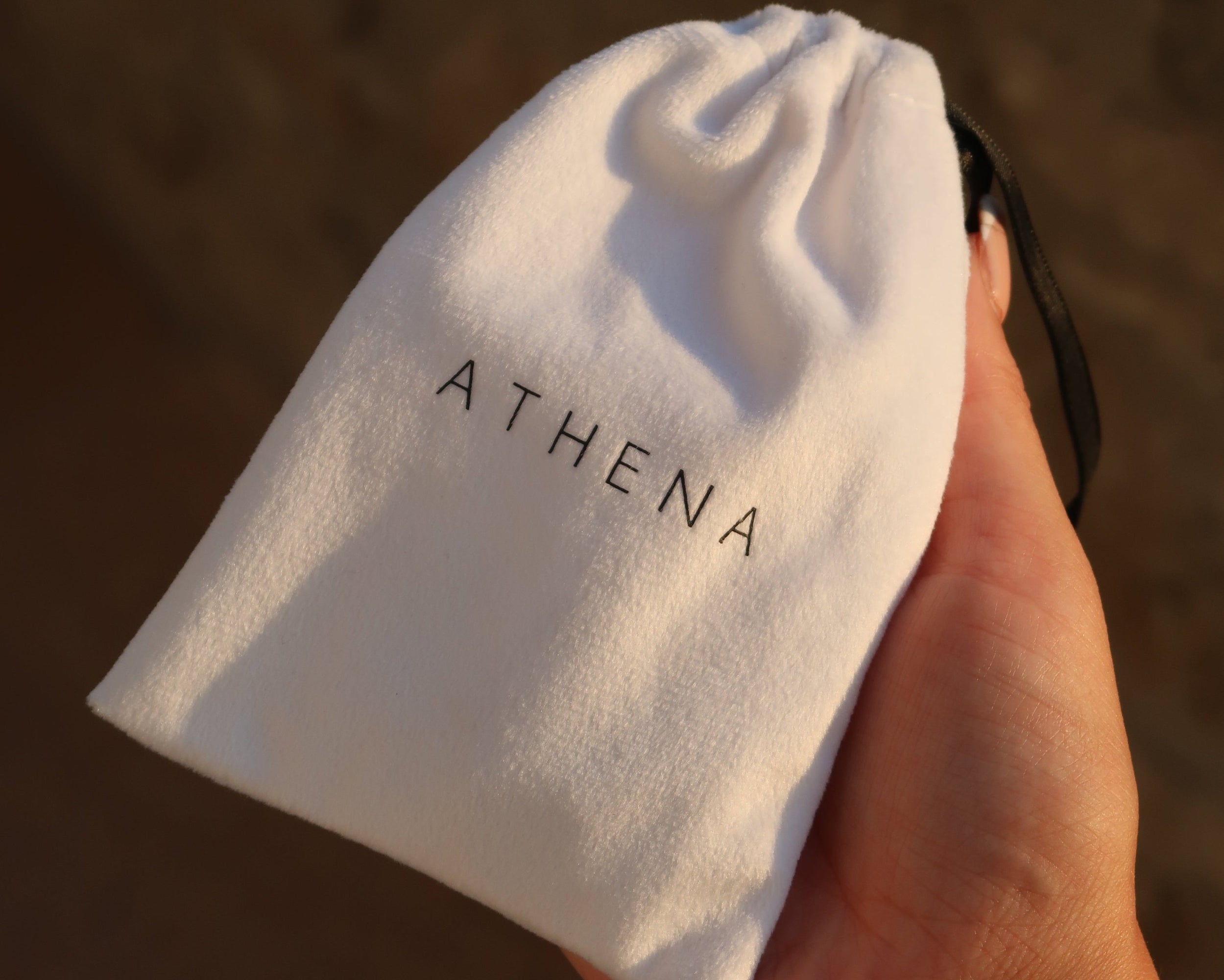 White velvet Athena Jewelry drawstring pouch held in hand showing luxury brand packaging