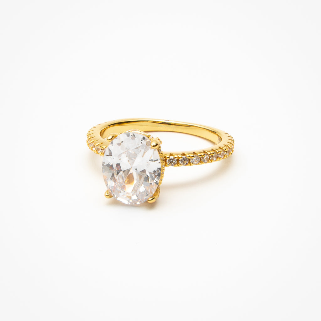 Oval cut cubic zirconia engagement ring with hidden halo and pavé band in yellow gold setting on clean white background showcasing brilliant center stone and sparkling details