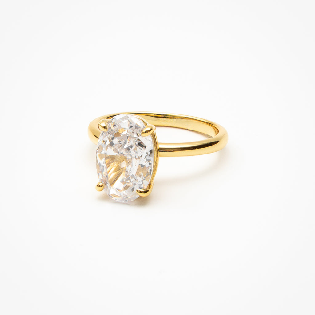 Oval cut cubic zirconia solitaire engagement ring in yellow gold setting on clean white background showcasing brilliant center stone and minimalist design