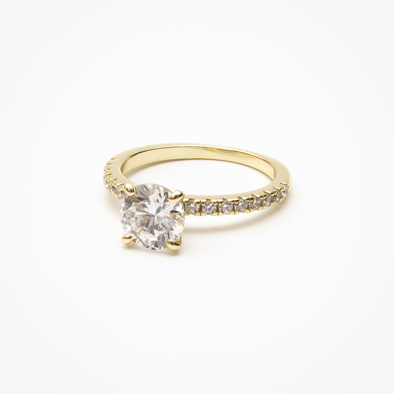 Round cut cubic zirconia engagement ring with pavé band in yellow gold setting on clean white background showcasing four-prong center setting