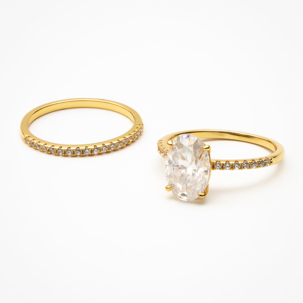 Oval cut moissanite engagement ring with pavé band and matching eternity wedding band in yellow gold setting on clean white background showcasing bridal set