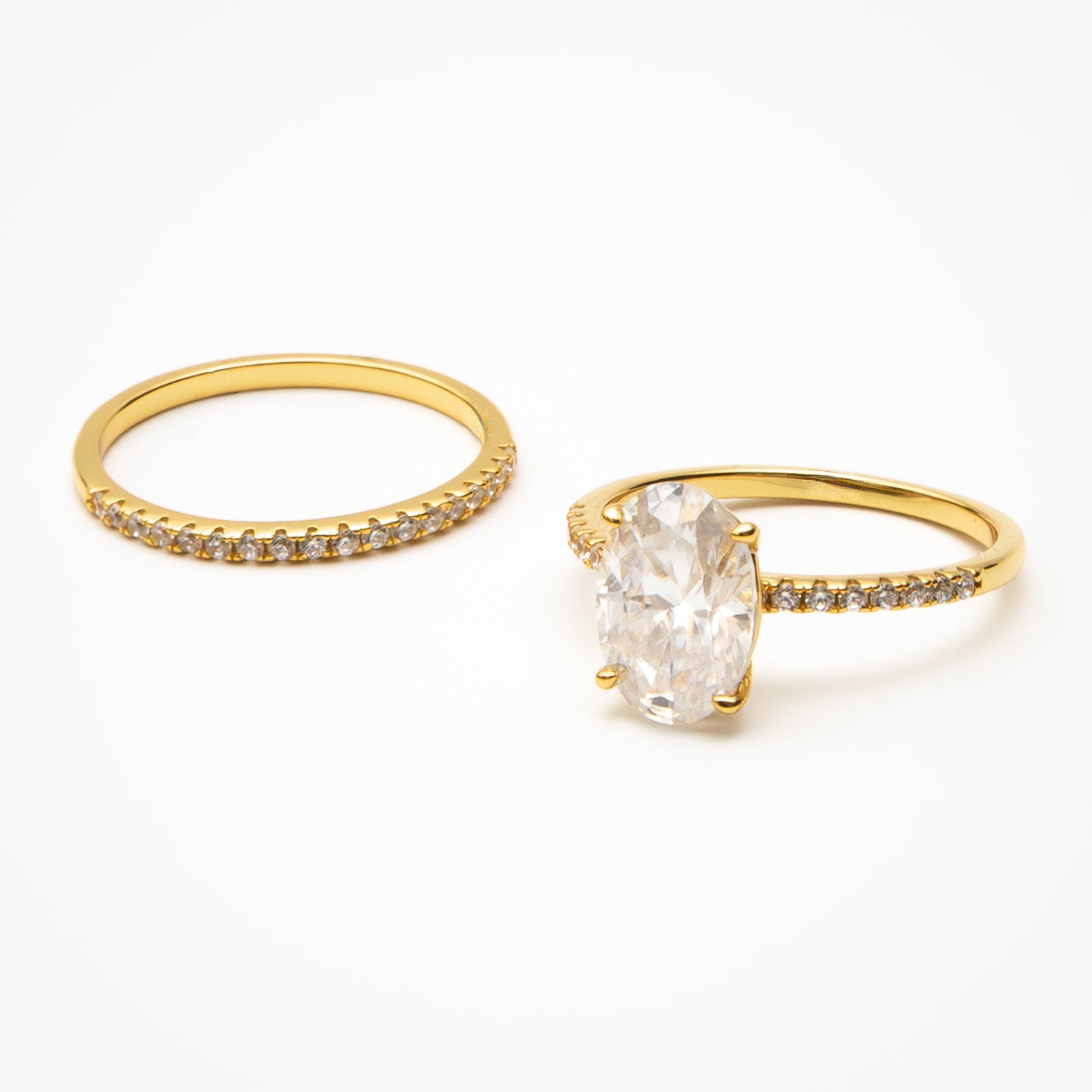 Oval cut moissanite engagement ring with pavé band and matching eternity wedding band in yellow gold setting on clean white background showcasing bridal set