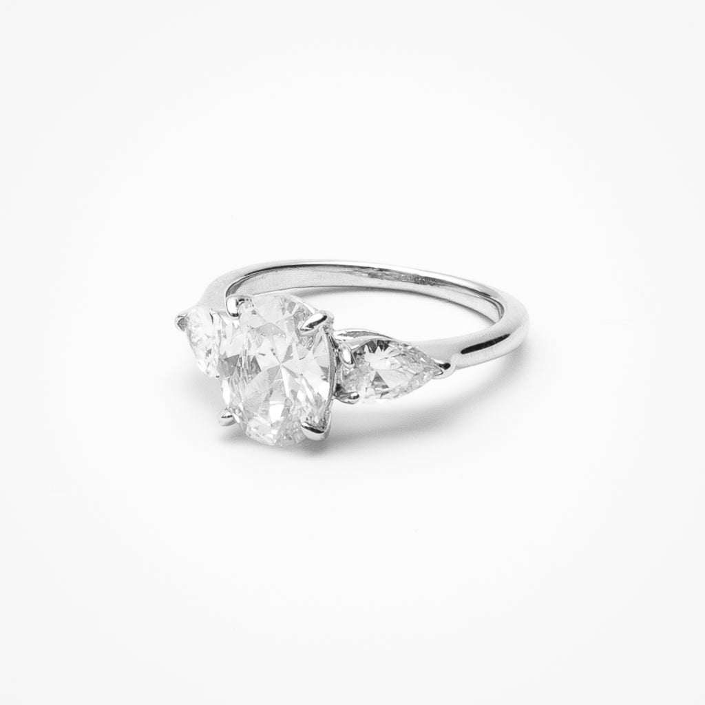 Oval cut cubic zirconia engagement ring with pear-shaped side stones in three-stone setting on white gold band against clean white background