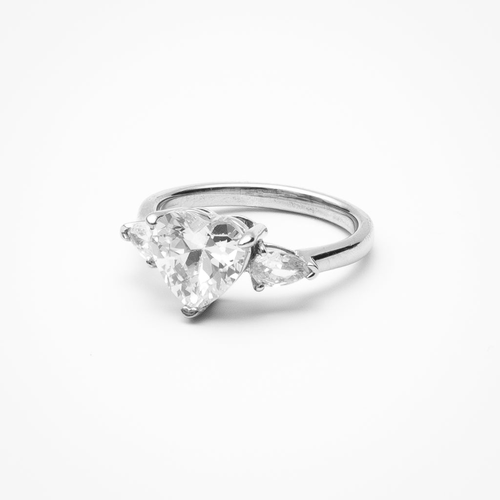 Heart cut cubic zirconia three-stone engagement ring with heart-shaped side stones in white gold setting on clean white background showcasing romantic design