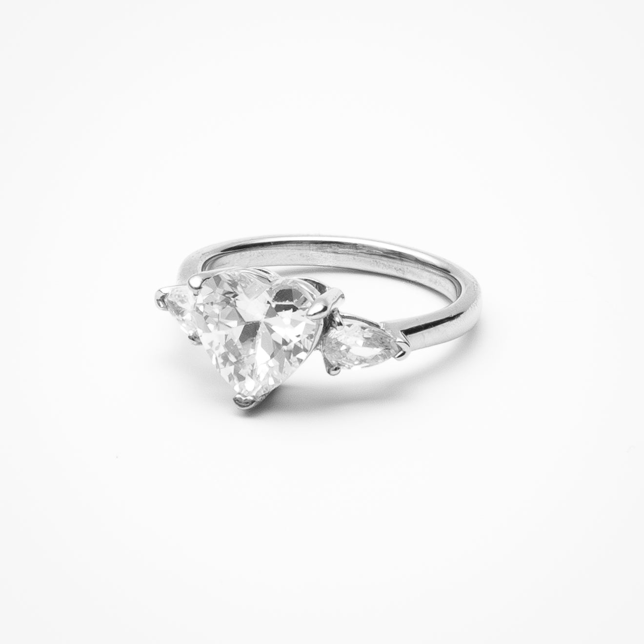Heart cut cubic zirconia three-stone engagement ring with heart-shaped side stones in white gold setting on clean white background showcasing romantic design