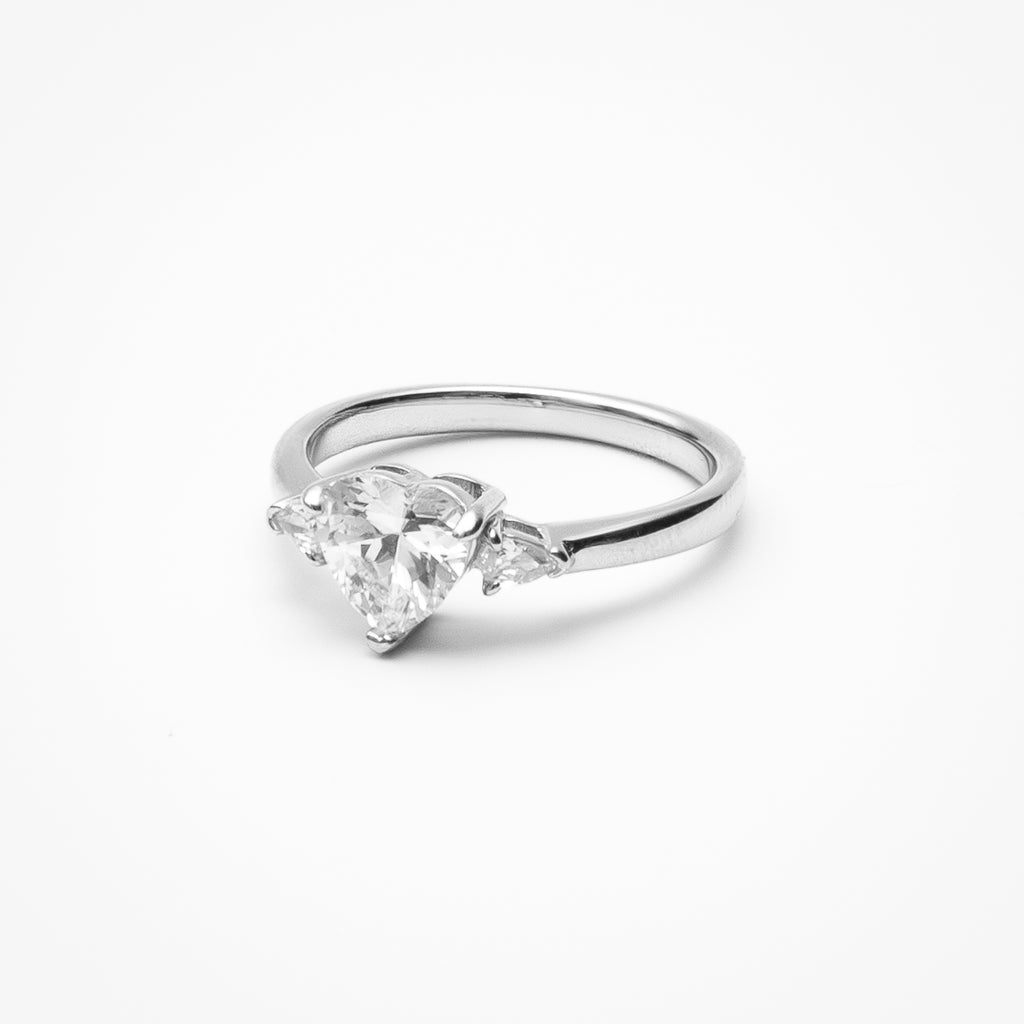 Heart cut cubic zirconia three-stone engagement ring with heart-shaped side stones in white gold setting on clean white background showcasing romantic design
