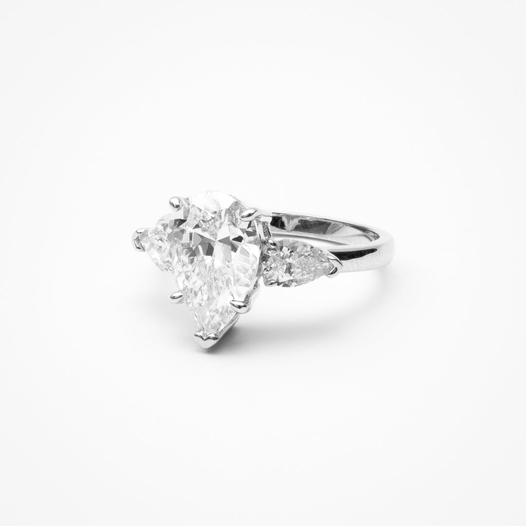 Pear cut cubic zirconia engagement ring with oval side stones in three-stone setting on white gold band against clean white background