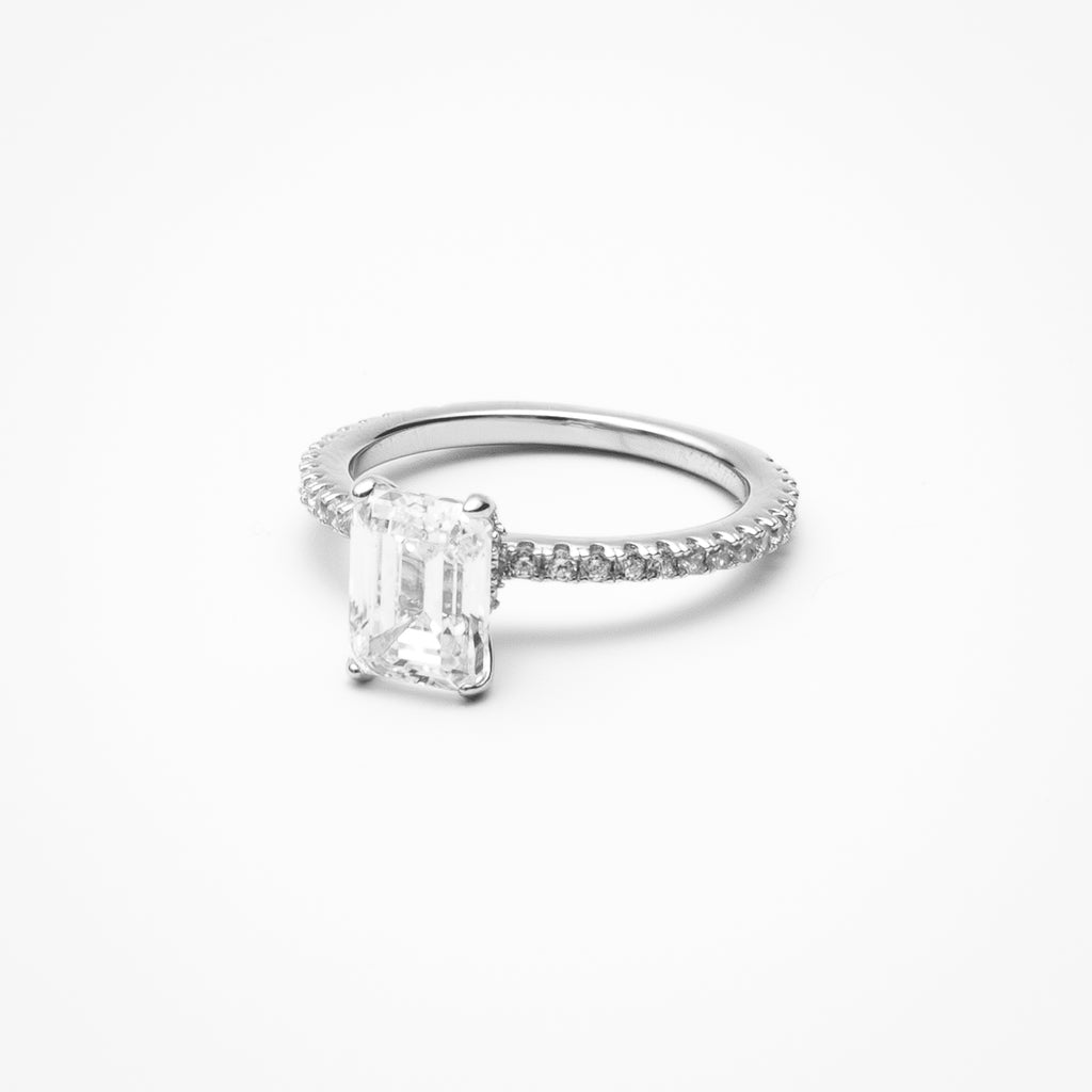 Emerald cut cubic zirconia engagement ring with pavé band and hidden halo in white gold setting on clean white background showcasing step cut faceting and raised setting