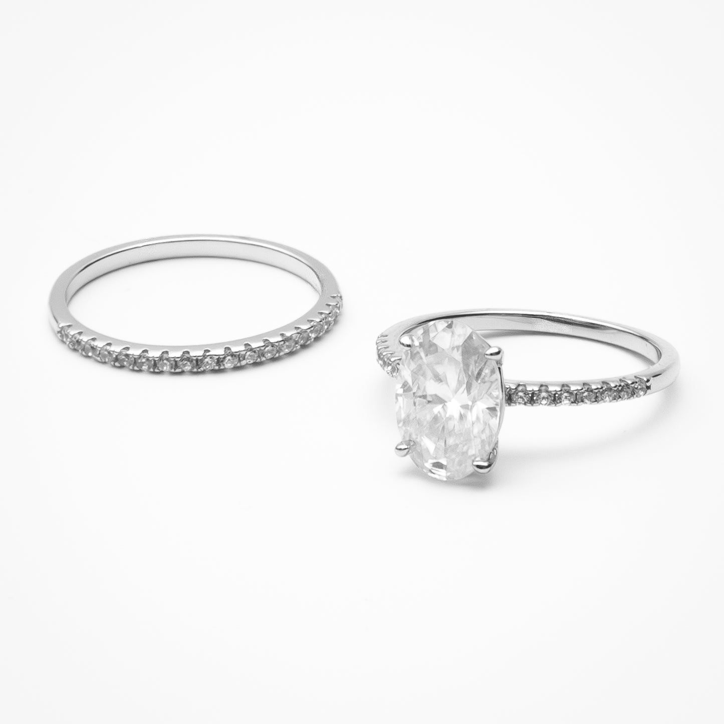 Oval cut moissanite engagement ring with pavé band and matching eternity wedding band in white gold setting on clean white background showcasing bridal set