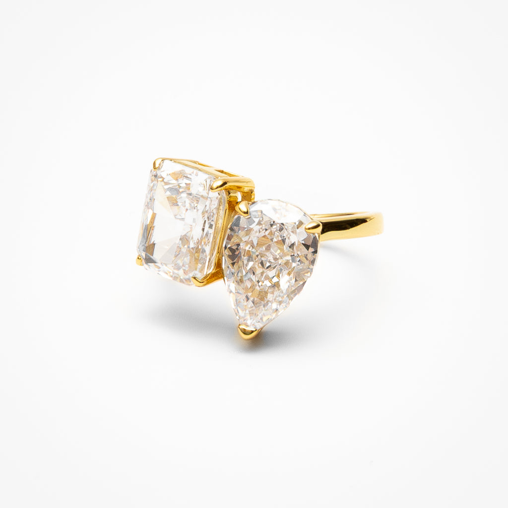 Toi et moi engagement ring with pear cut and radiant cut cubic zirconia stones in yellow gold setting on clean white background showcasing dual stone design
