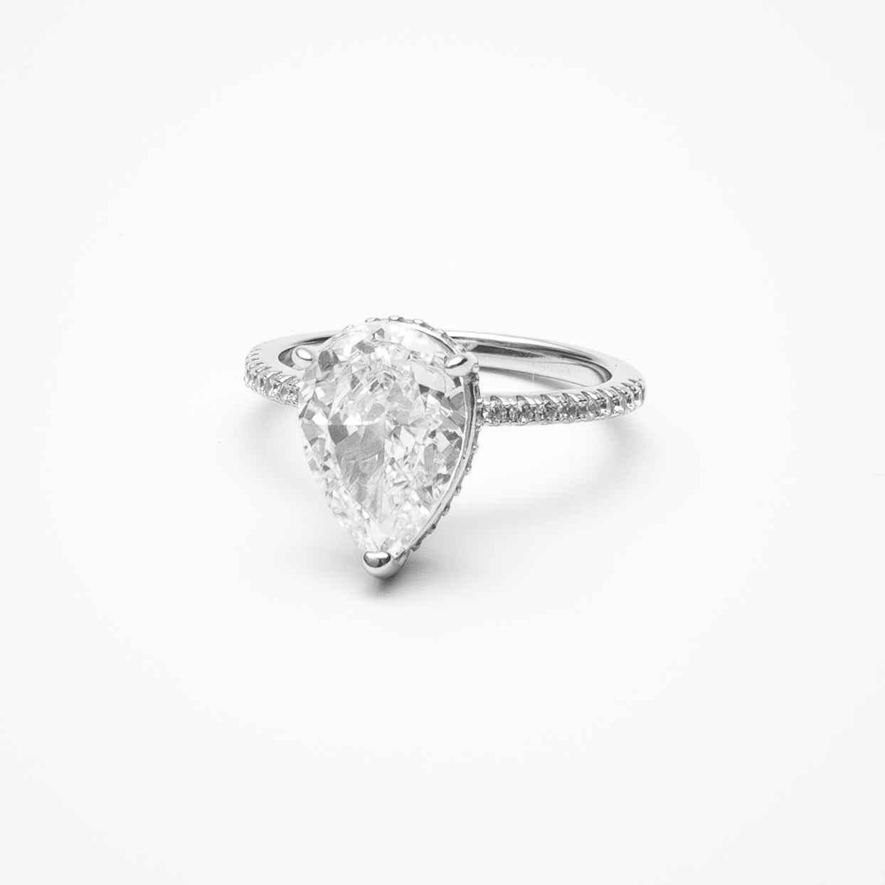Pear cut cubic zirconia engagement ring with hidden halo and pavé band in white gold setting on clean white background showcasing teardrop shape and sparkling details