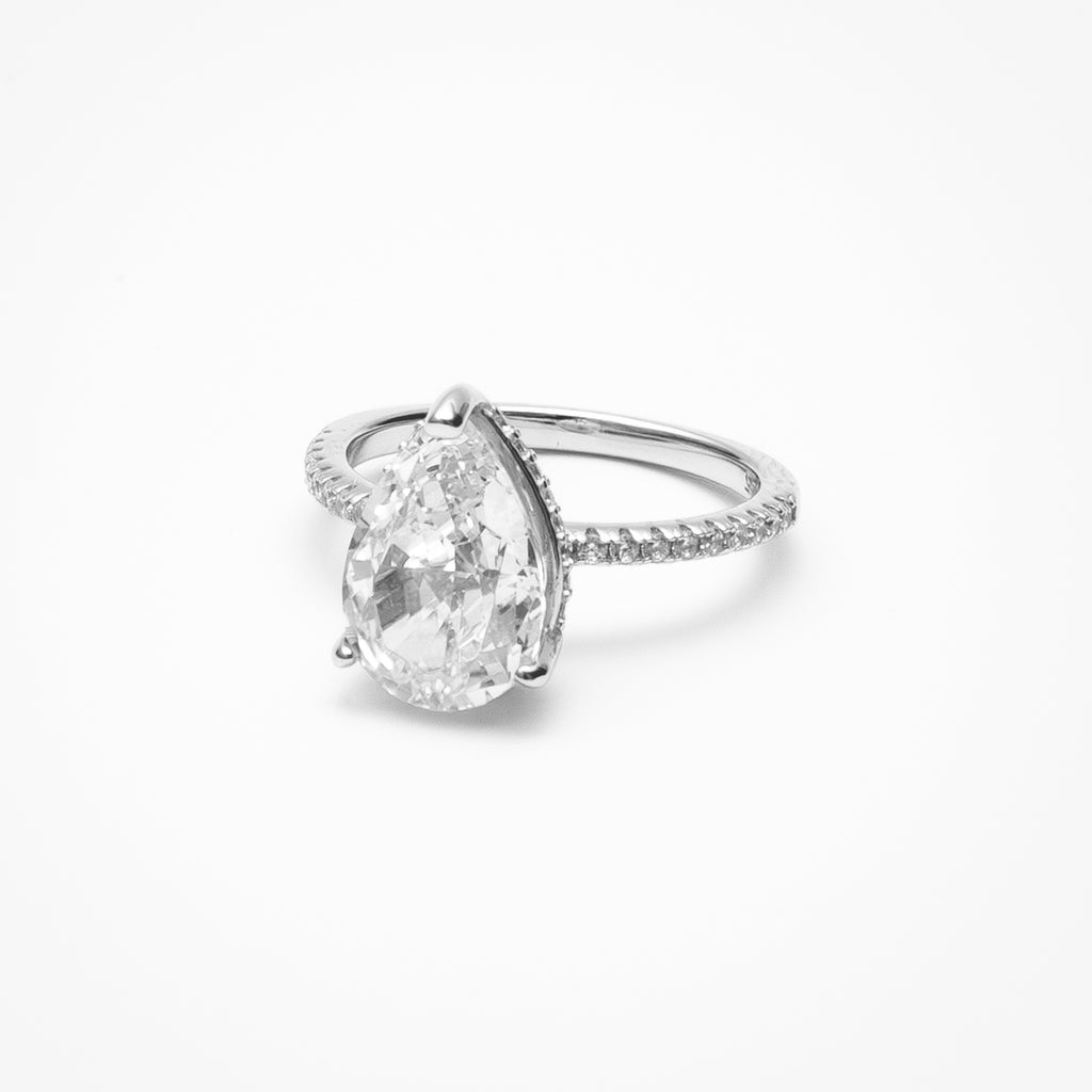 Pear cut cubic zirconia engagement ring with hidden halo and pavé band in white gold setting on clean white background showcasing teardrop shape and sparkling details