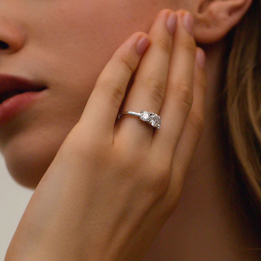 Close-up of hand with round cut moissanite three-stone engagement ring showing elegant profile and stone arrangement