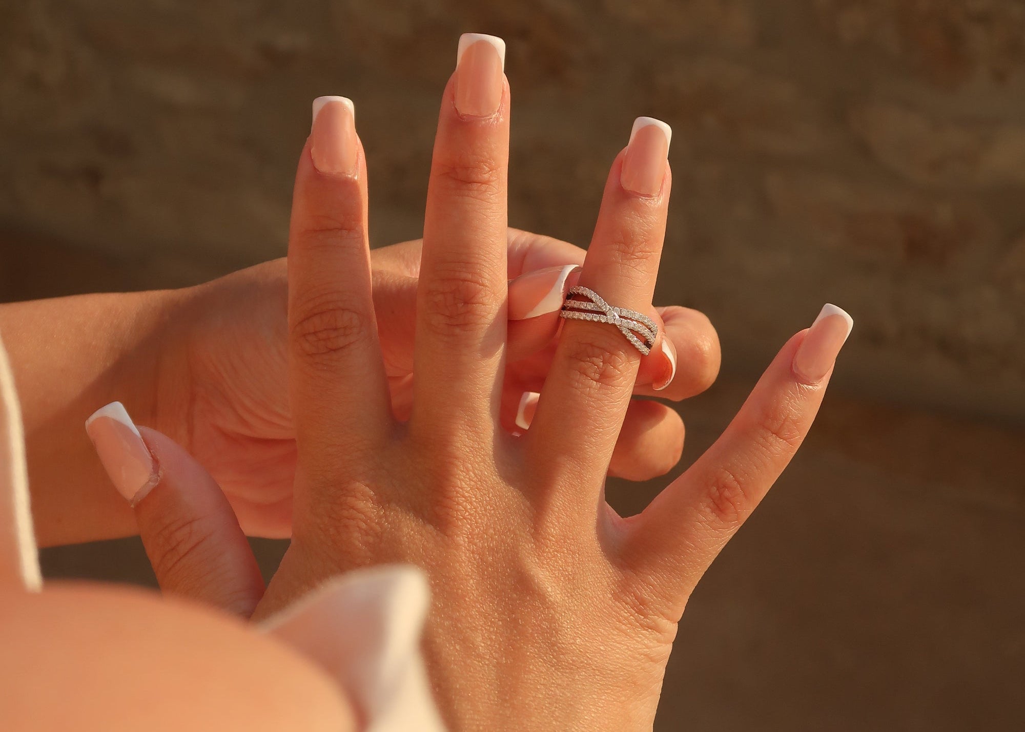 Moissanite twisted band ring worn on ring finger with French manicure nails in warm natural sunlight