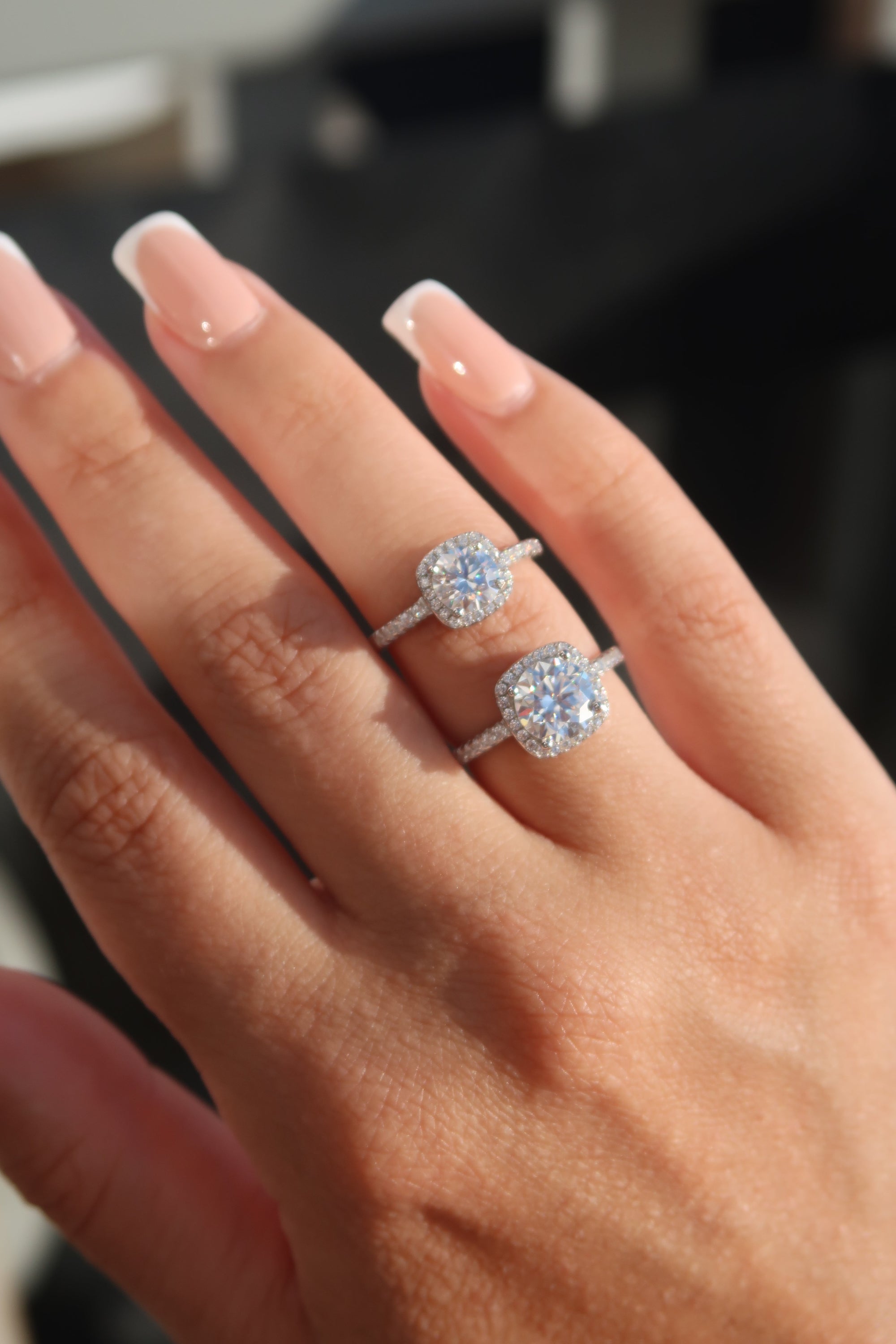 Two matching moissanite halo engagement rings with round brilliant center stones and pavé diamond bands worn on ring finger with French manicure
